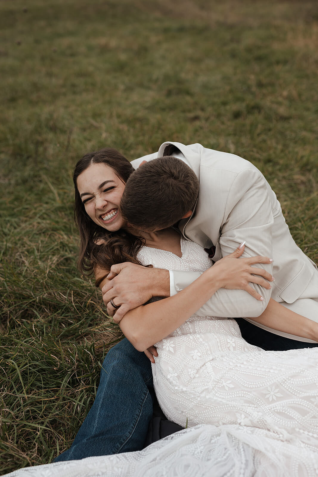 Groom hugging his bride from behind while both smile at the camera during Lancaster Wisconsin farmhouse wedding portraits