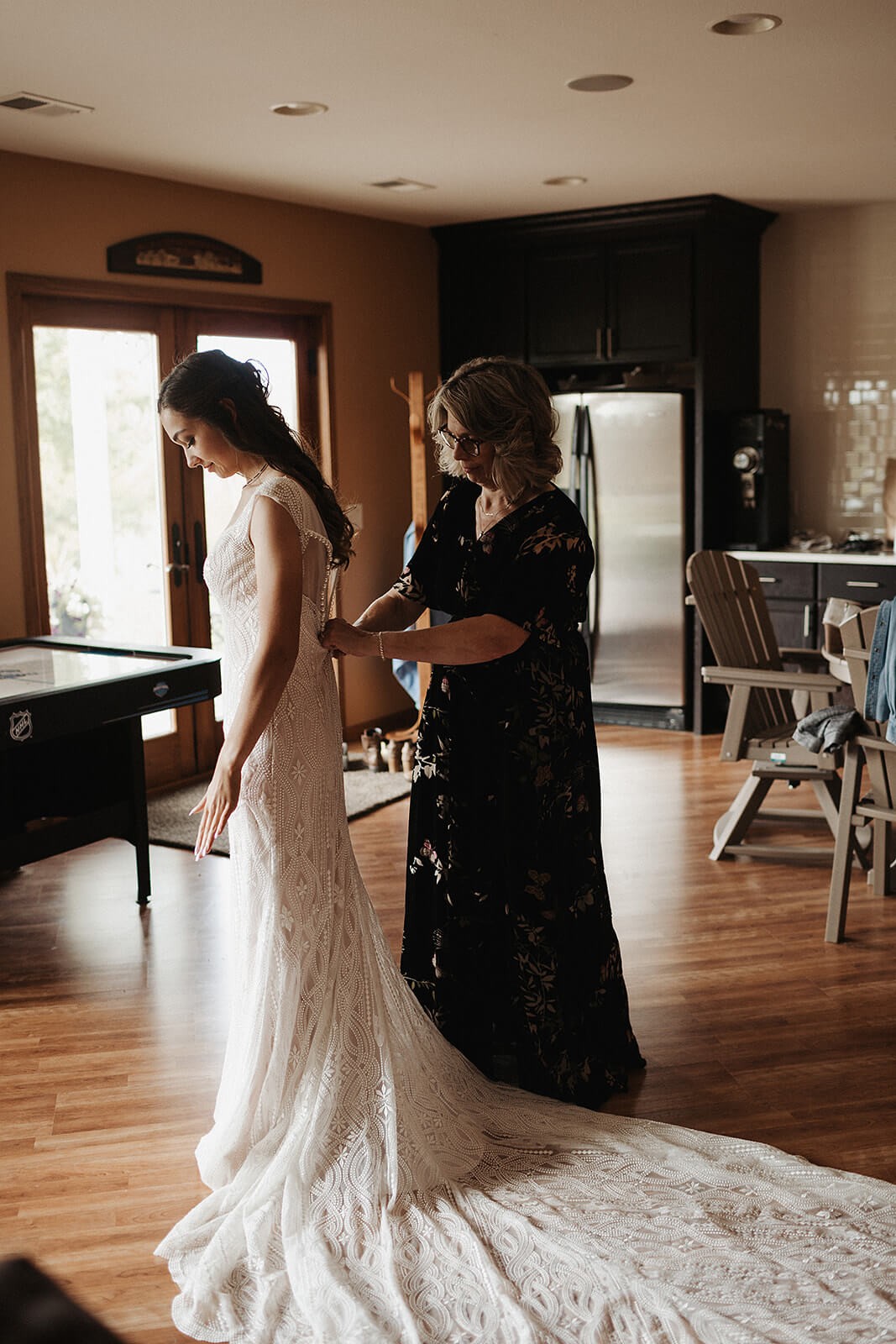 Mother of the bride fastening the back of a lace wedding dress in the living room of a Lancaster Wisconsin family home on the morning of the wedding