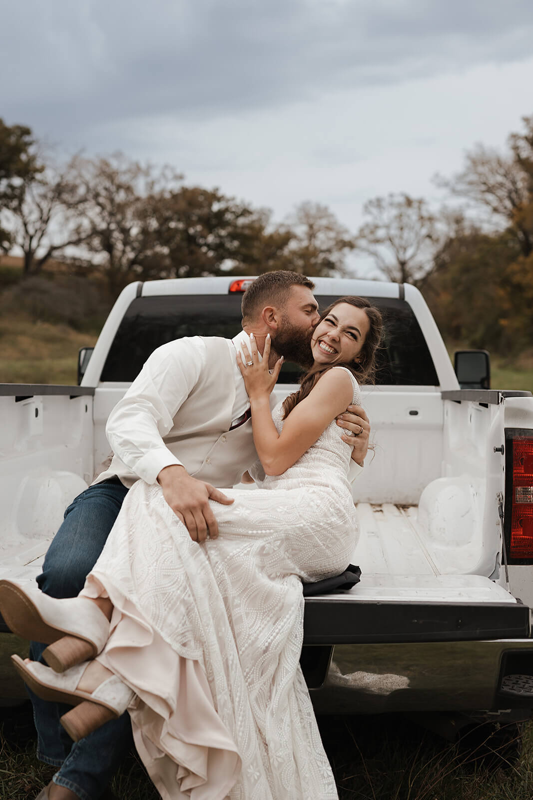 Bride and groom sitting together in the bed of a pickup truck during relaxed Lancaster Wisconsin wedding portraits