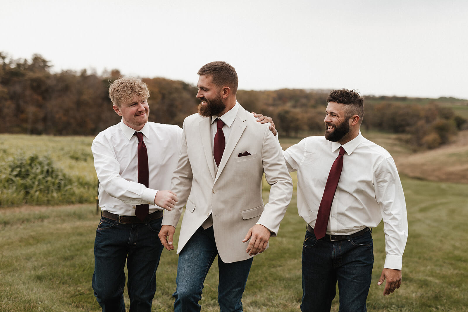 Groom and groomsmen laughing together while walking through a green farm field during a Lancaster Wisconsin wedding