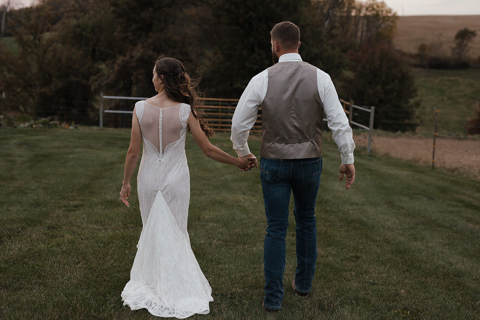 Groom leading his bride by the hand through a wide open green field with rolling hills in the background during Lancaster Wisconsin wedding portraits
