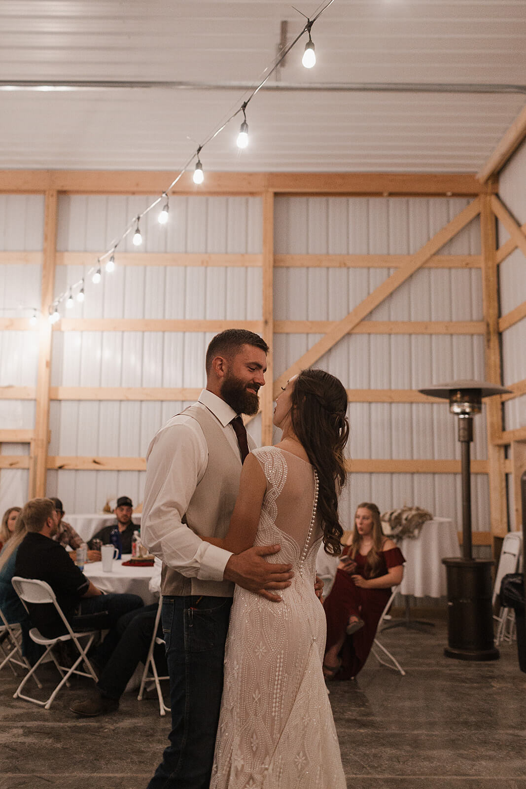 Bride and groom looking at each other during their first dance inside a warmly lit barn at a Lancaster Wisconsin farmhouse wedding reception