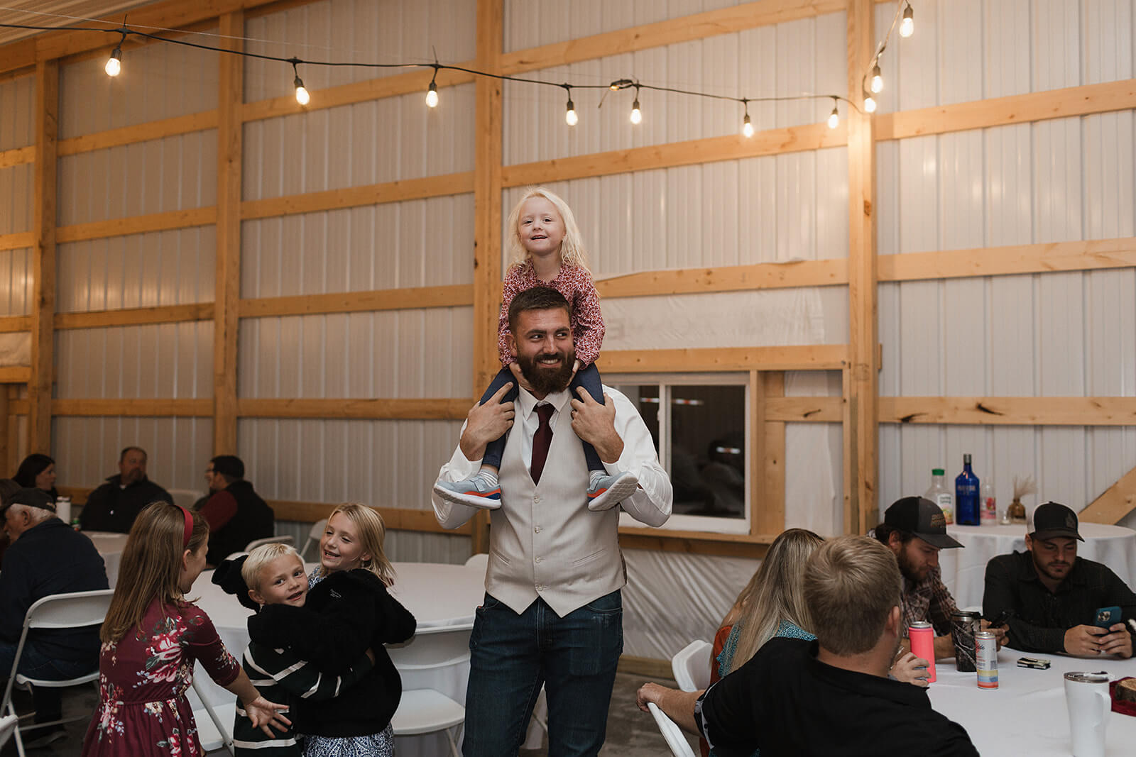 Groom carrying a young child on his shoulders while guests celebrate on the dance floor during a Lancaster Wisconsin barn wedding reception